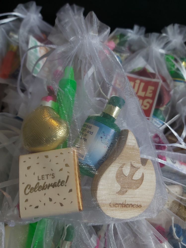 Goody bag for adults in the service.
White organza bag holding a wooden flame engraved with gentleness, party popper, bubbles, fizzy sweets, heart chocolate and a let's celebrate chocolate. 