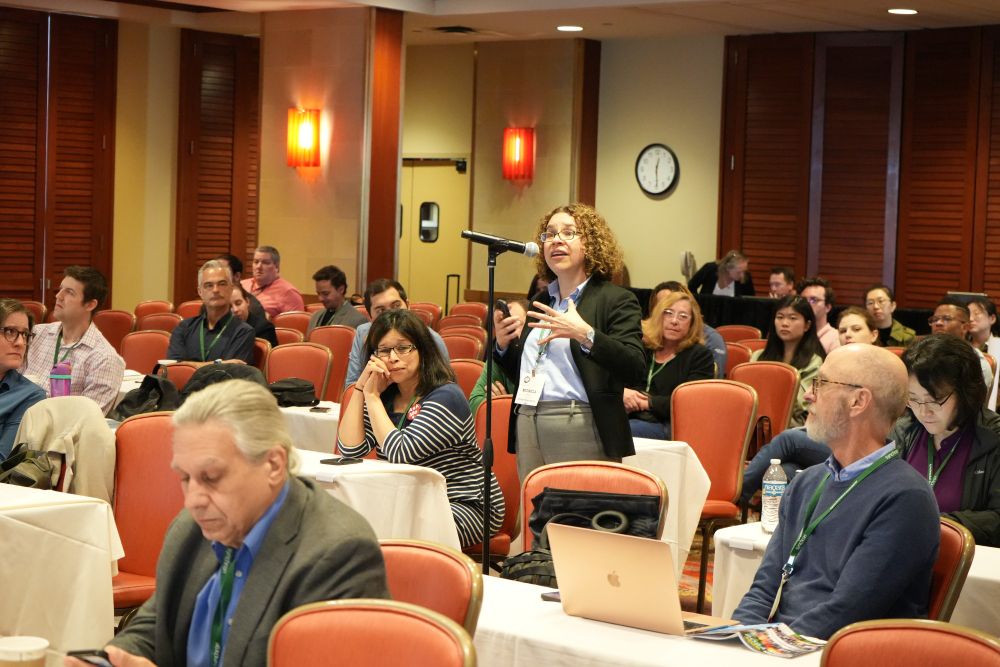 A member of the audience is standing at a microphone addressing the panel.