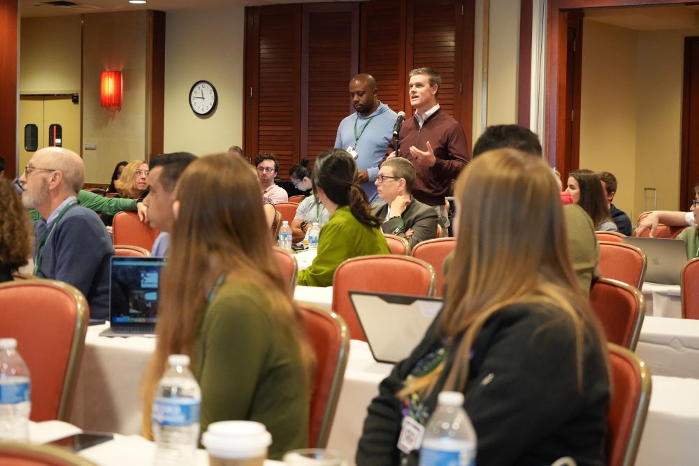 A member of the audience is standing at a microphone addressing the panel.