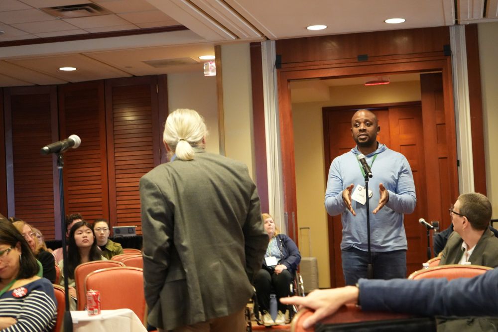 A member of the audience is standing at a microphone addressing the panel.