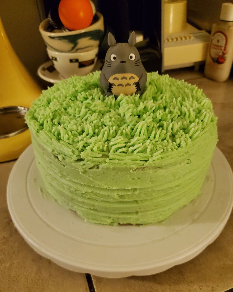 A cake frosted in green to look like there's grass on top, with a 3D printed Totoro figurine in the middle 