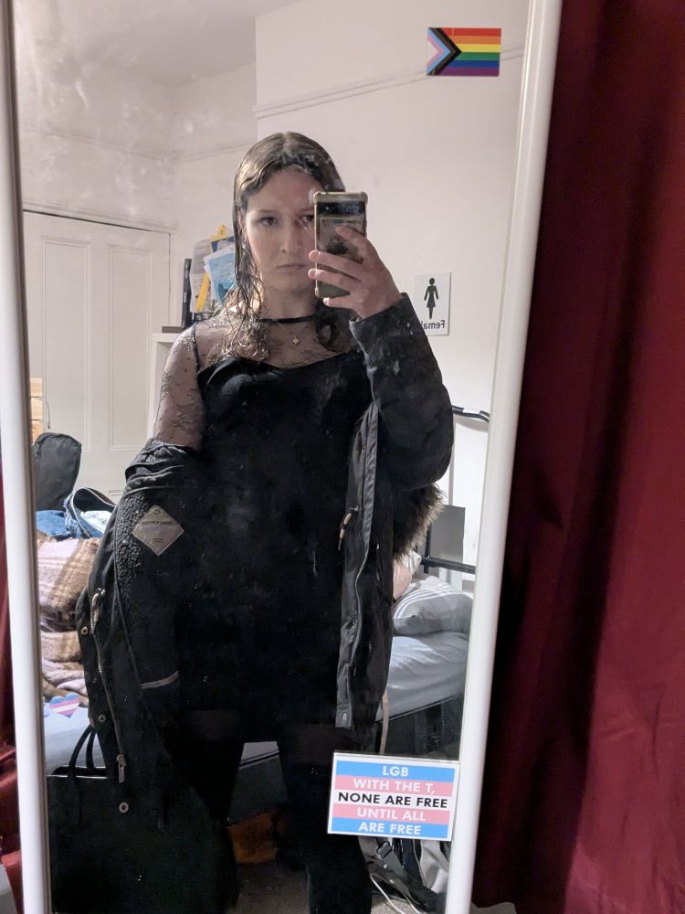 a selfie in the mirror, I am wearing a black dress and coat and holding my handbag