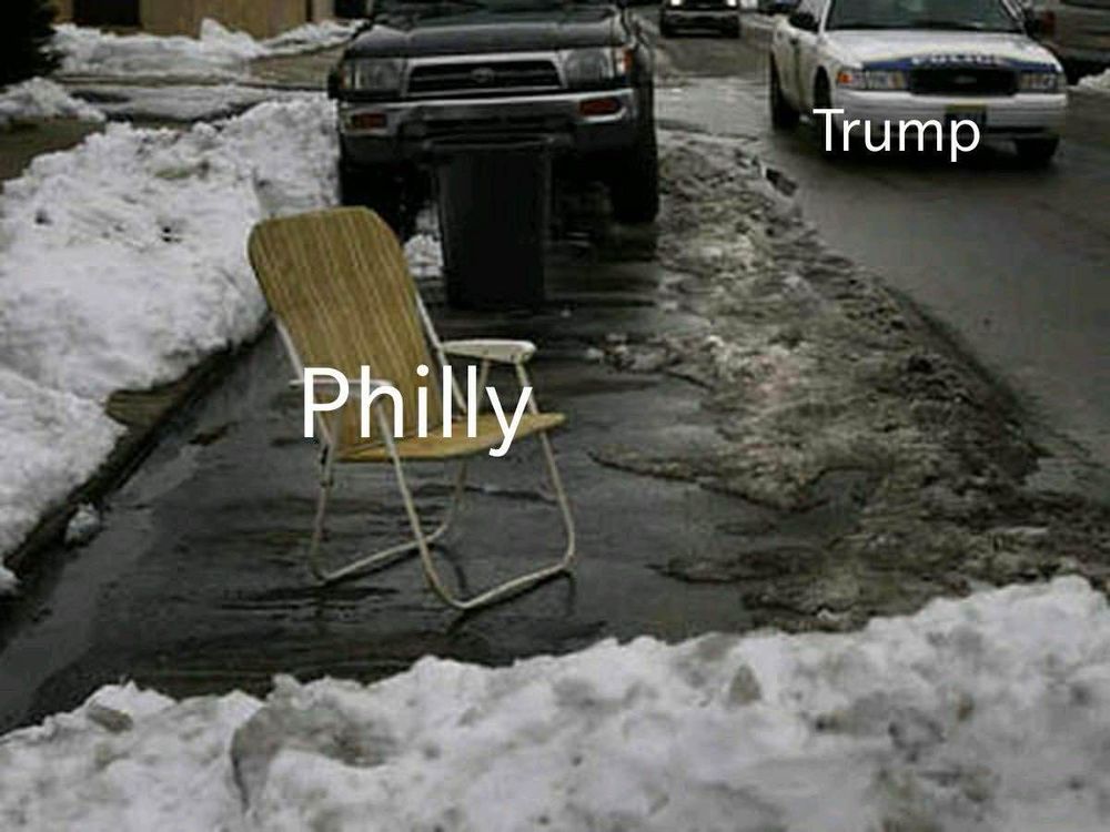 Meme image of a car trying g to park on a slushy street. There’s an open spot being blocked by a lawn chair. The car is labeled Trump, the chair is labeled Philly. 
