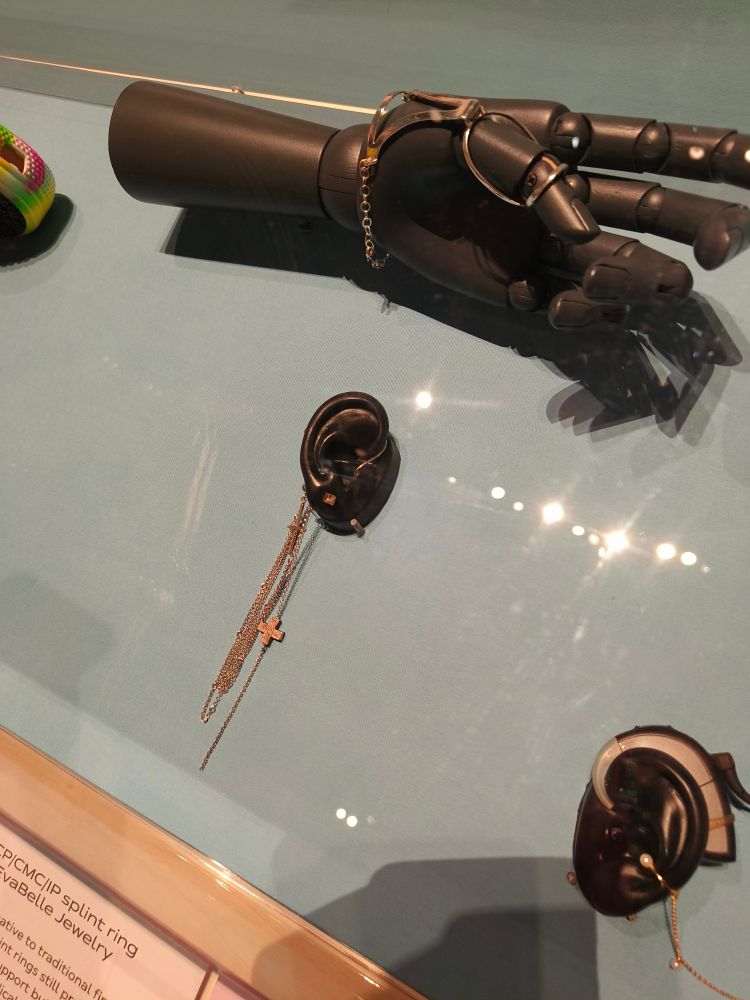 Photo of a splint ring on a hand and a 'Death Metal' hearing aid jewellery 

"Jenni Ahtiainen created accessories for hearing aid user struggling with stigma when she starts using hearing aids herself. She processed this change by customising her own hearing devices, transforming medical kit into stylish jewellery. Her accessories create an important opportunity for choice, allowing users to celebrate their access aid or make it more discreet.'