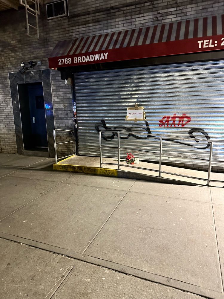 a photograph of shuttered bagelry, with a bouquet of flowers left at the door