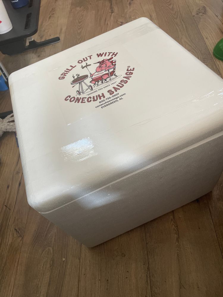 A photo of a white foam cooler with a “grill out with conecuh sausage” sticker on top