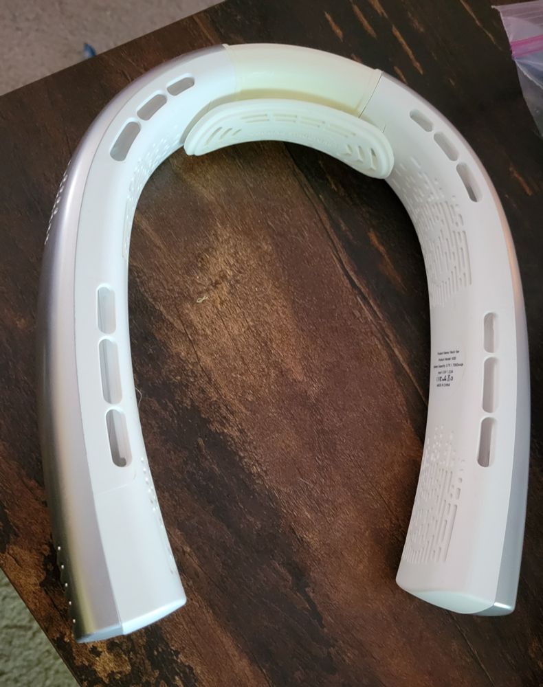 A white neck fan is shown on a tabletop. The fan is u-shaped with small vents along its sides.