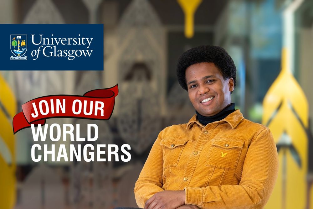 Image shows JMS Scholar Adam Heron sitting to one side with his arms crossed, wearing a golden shirt and smiling at the camera