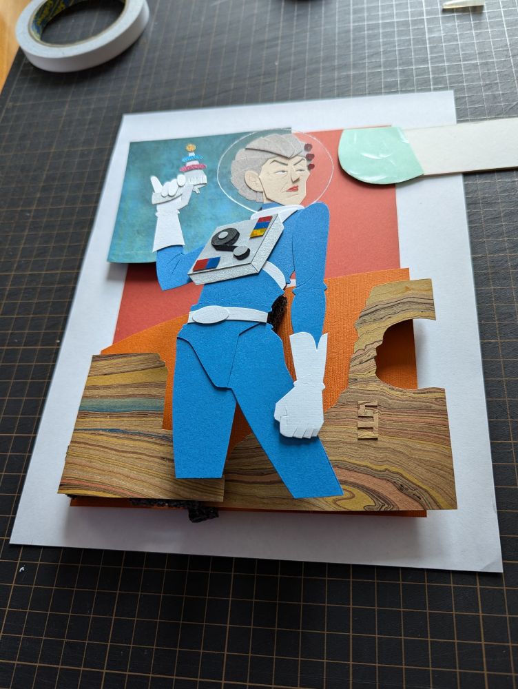 Wide shot of the paper illustration showing it on a cutting mat on a table, to show the scale and height.