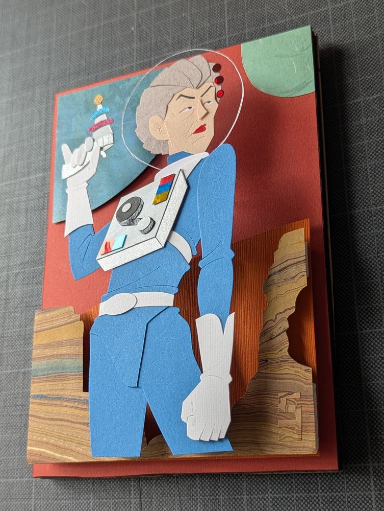 A photo of the paper illustration from a slight angle, the illustration now having been cut down on all sides in order to fit into a deep, shadow box frame.
