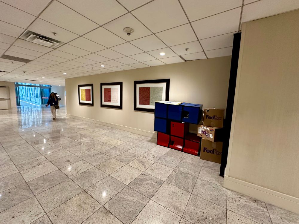 A stack of Tetris-style cardboard boxes in the Fed Ex Jon corner (Blessed be the Route; Under His Googly Eye; Must Be 18, &c.), along with other Dragon Con-related paraphernalia on Monday, 8 Sept 2025