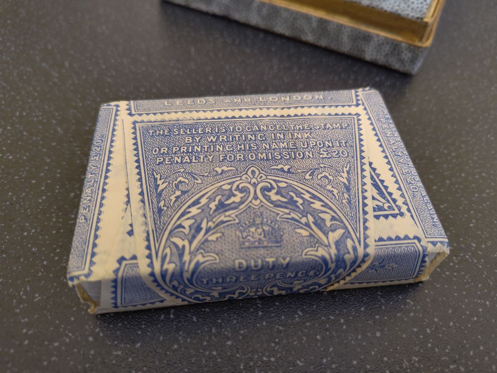 The wrapped deck. The paper says "The seller is to cancel the stamp by writing in ink or printing his name upon it. Penalty for omission £20. Duty three pence"