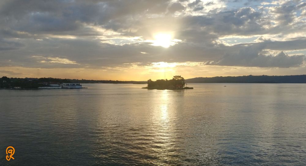 Looking at a Summer sunset from Isla Flores, Guatemala. Cloudy, but golden skies illuminate the lake. Only to be interrupted by Islote Santa Bárbara. A natural splendor in preparation to celebrate an anniversary.
