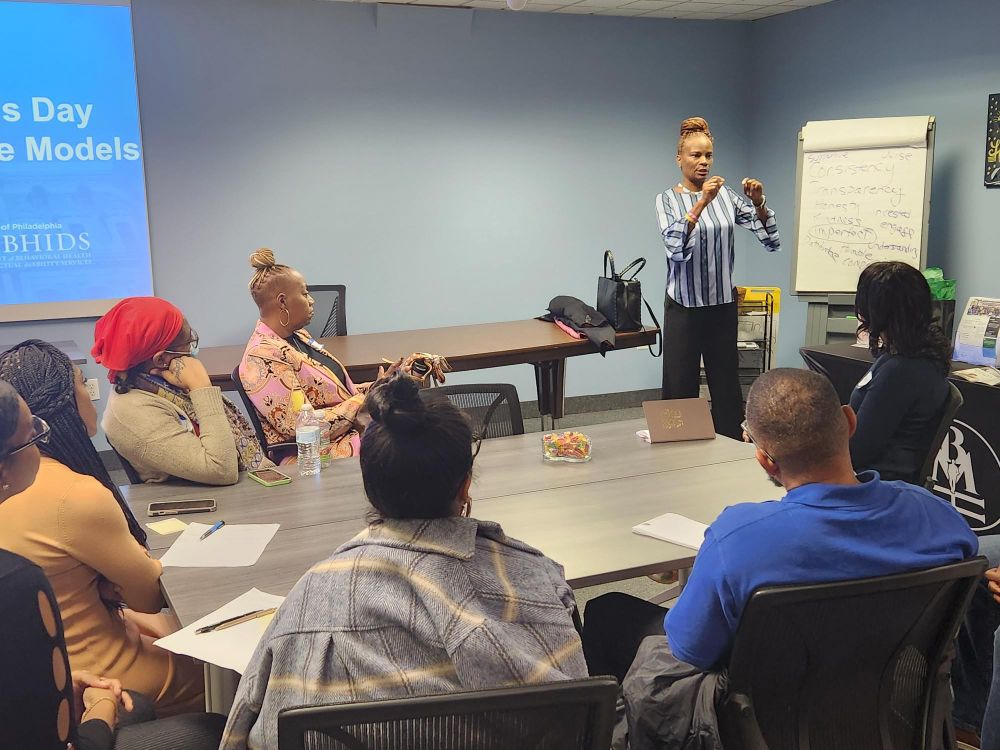 Speakers and audience as part of the annual DBHIDS celebration of International Men's Day. The 2024 theme is Positive Male Role Models. In this photo, a female speaker addresses the audience.