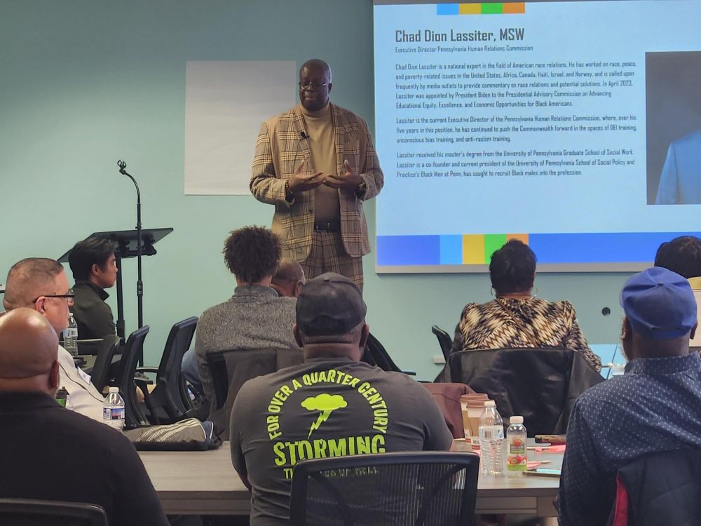 Speakers and audience as part of the annual DBHIDS celebration of International Men's Day. The 2024 theme is Positive Male Role Models. In this photo, Chad Dion Lassiter addresses the audience.