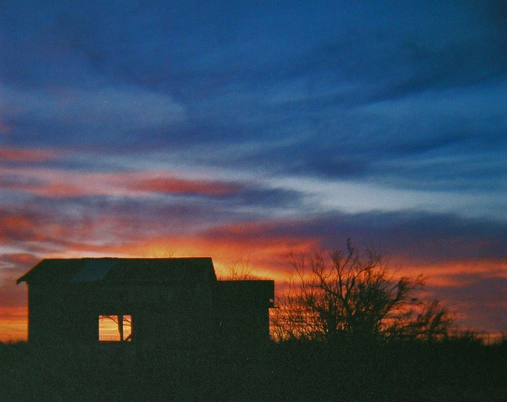 dusk shot of an old house ruin in silhouette, the colors of the sunset showing through a window