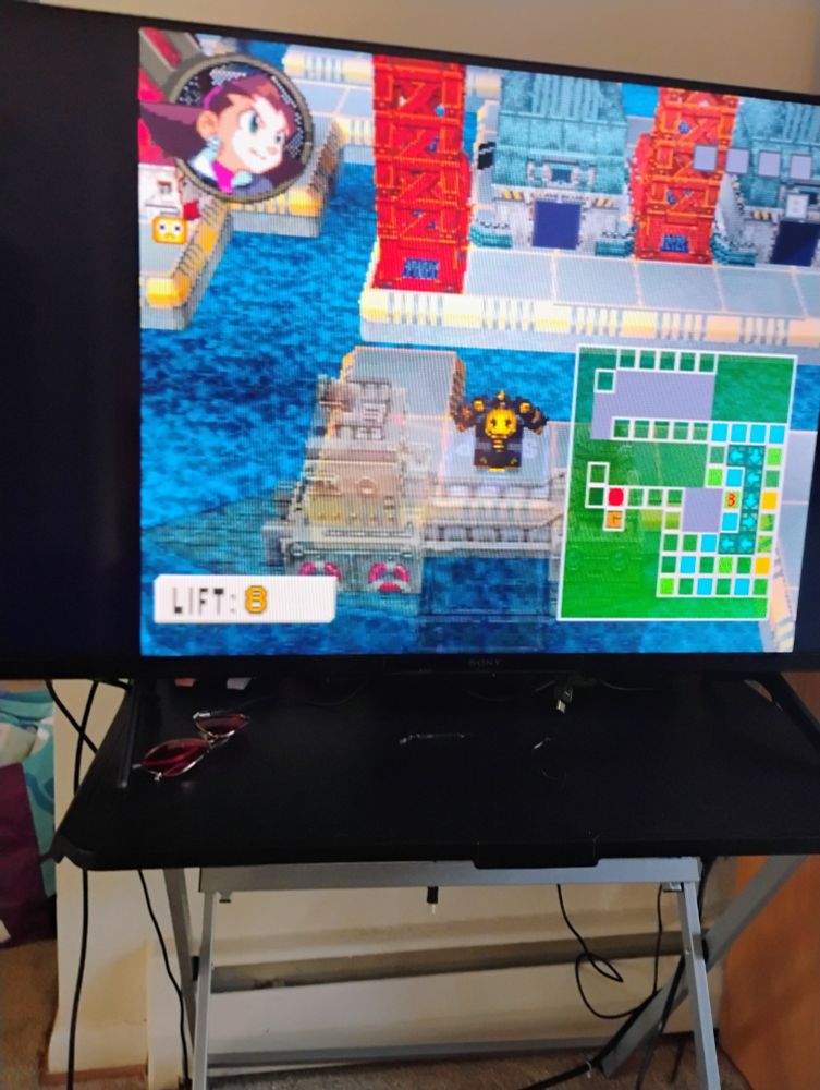 Scene from The Misadventures of Tron Bonne for the Sony PlayStation (PS1 or PSX) in a flat screen TV, where Tron's darky themed machine has to navigate a harbor full of crates. The corner shows a grid.