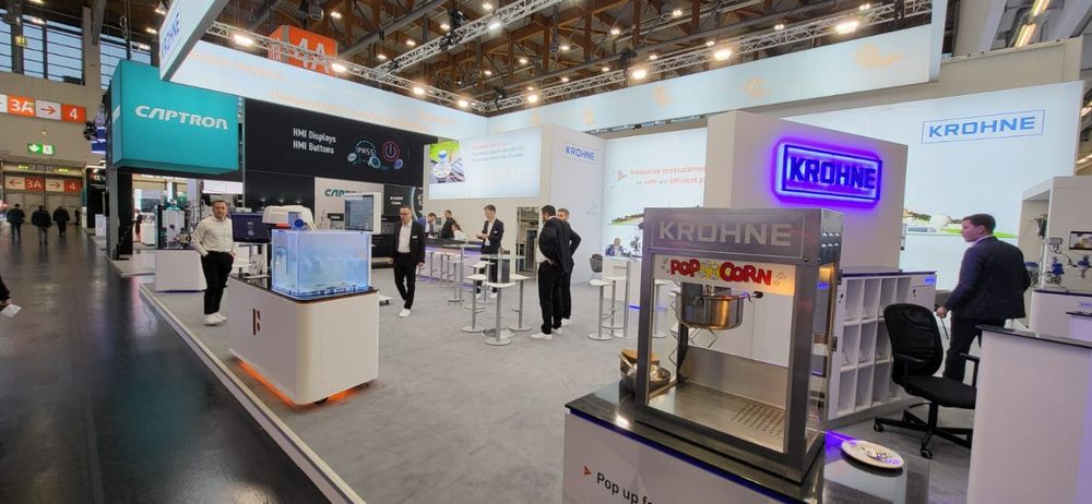 Dies ist eine Ausstellungsfläche mit Produkten und Mitarbeitern der Firma Krohne, einem Anbieter von Messgeräten und Industrieausrüstung.