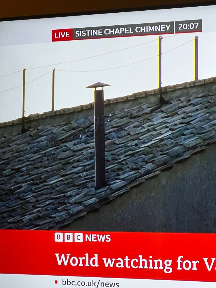 A photo of a TV screen showing a livestream of the chimney at the Sistine Chapel with no smoke coming out of it. 