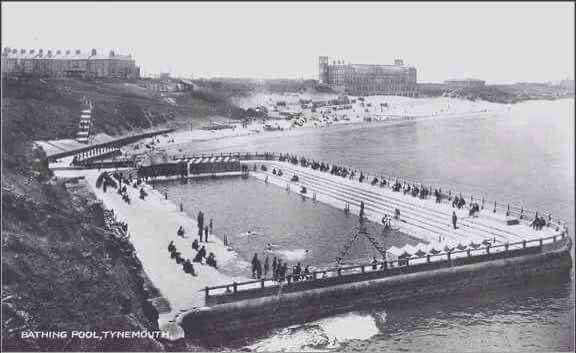 A historic picture of a large open-air swimming pool, surrounded by terraces and sea wall, set on a long, sandy beach.