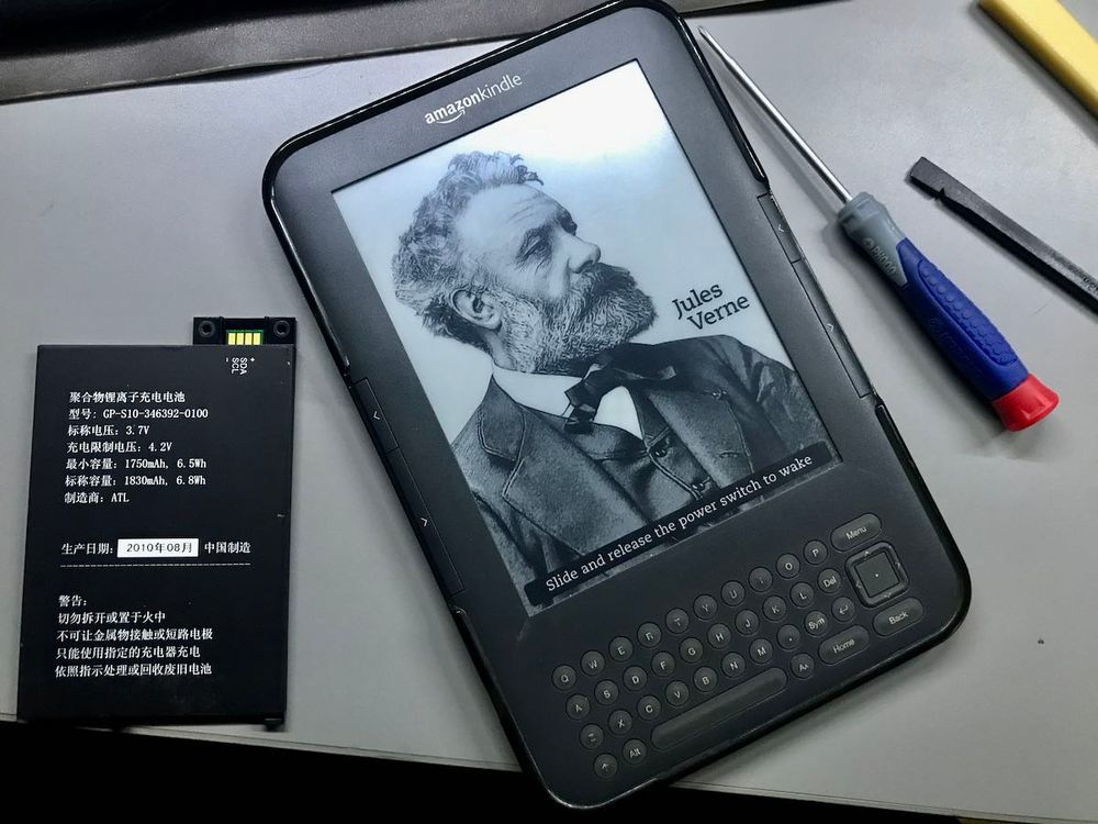 Image of a Kindle (showing Jules Verne) on a table with tools around it. Source: https://swling.com/blog/2021/01/reviving-a-kindle-hacking-a-nook-and-more-e-ink-please/