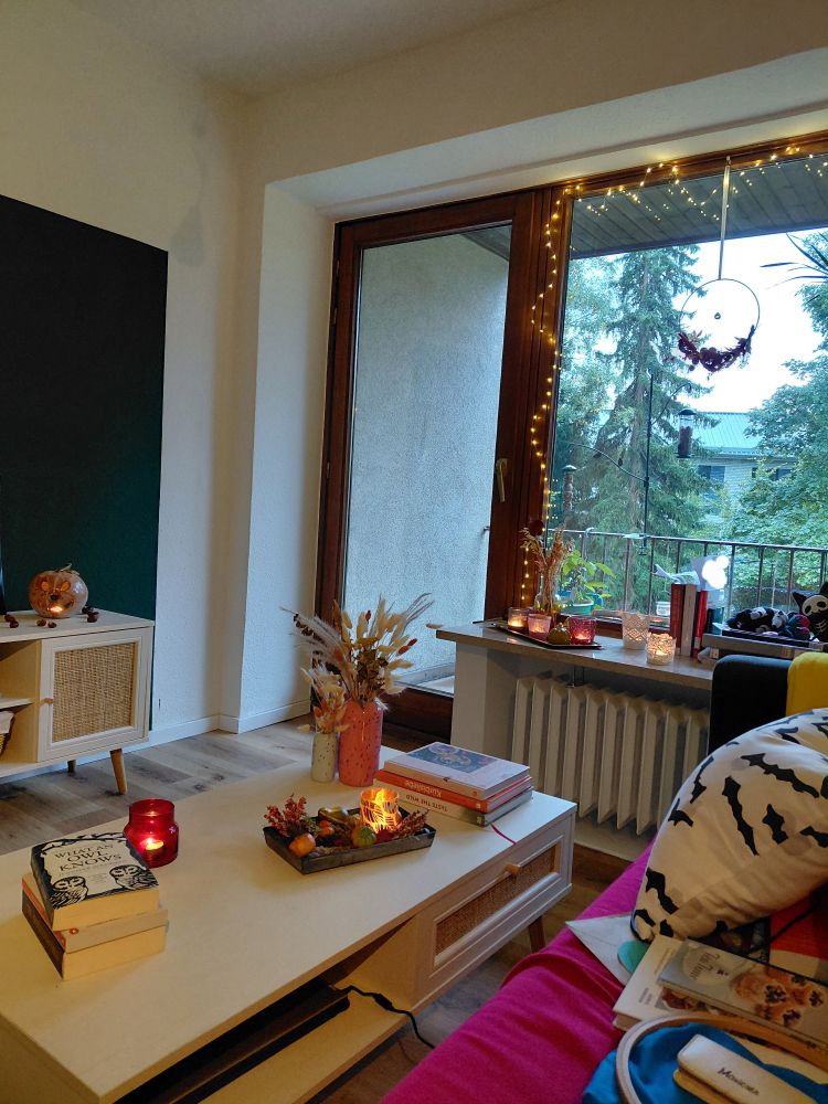 Foto aus meinem Wohnzimmer, Blick auf den Balkon, graues Wetter. Couchtisch und Fensterbank mit Büchern, brennenden Teelichtern und Herbstdeko.