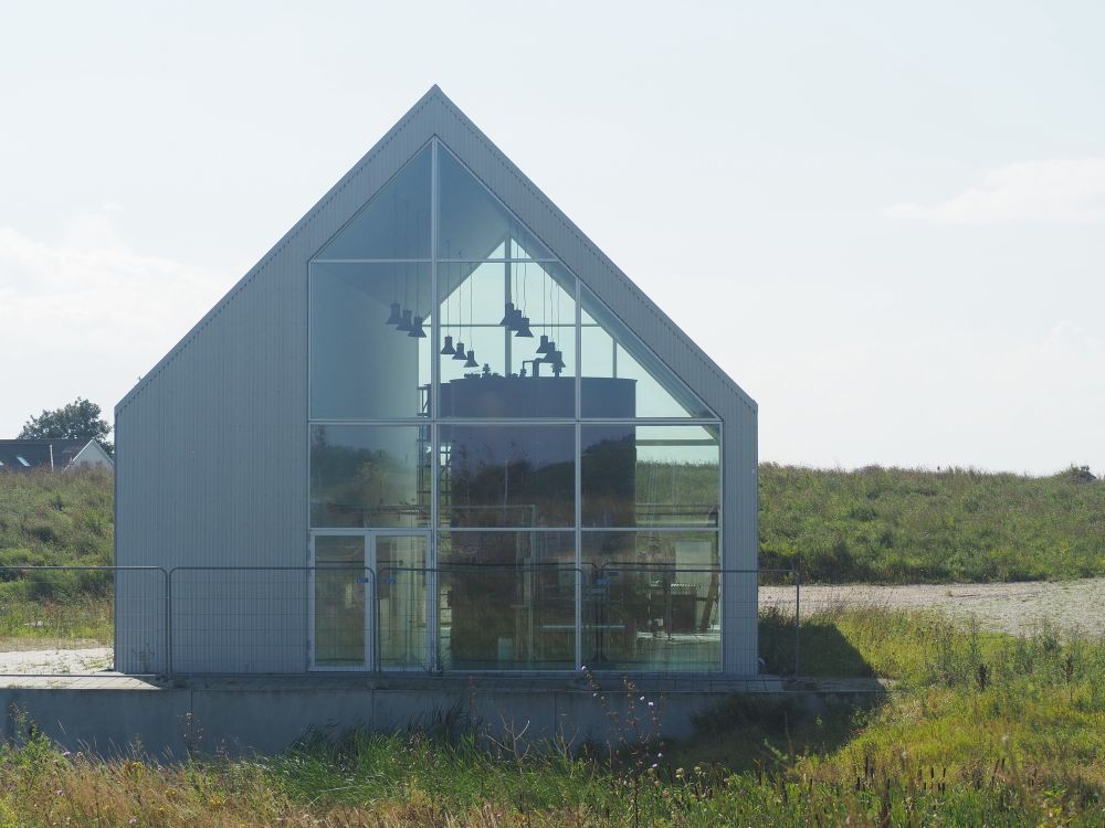 Photo of glass wall on an A-frame building near a pond with grass growing around it