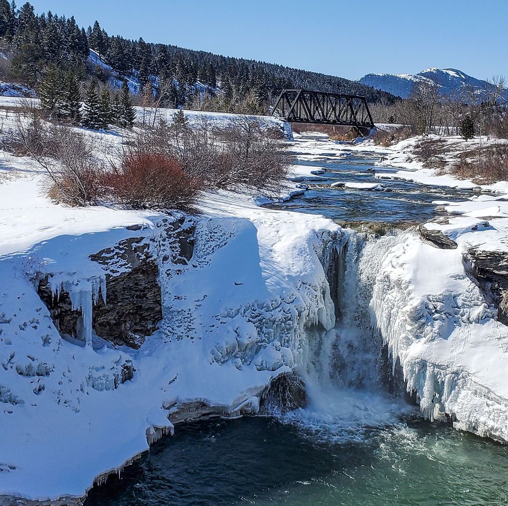 Partially frozen waterfall on a small river with mountains raising in a distance. 