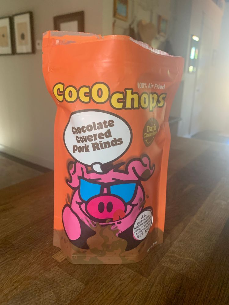 An orange bag that says Coco chops. Is chocolate covered pork rinds there’s a pig with sunglasses on the bag.