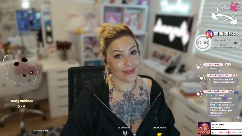 Streamer Crunchess smiling and looking at the camera while sitting in front of her desk, featuring a cozy and playful background. Her tattoos are visible as she sports a hoodie. The screen displays an overlay with daily sub count, chat messages, and a Pomodoro timer, with a cute animated Pikachu in the corner.