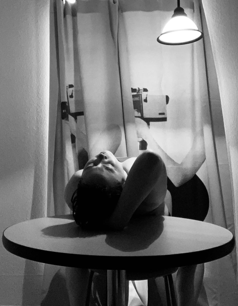 An Asian person leans back over a round table in the same position as Weems in the preceding image.There is a curtain behind them.