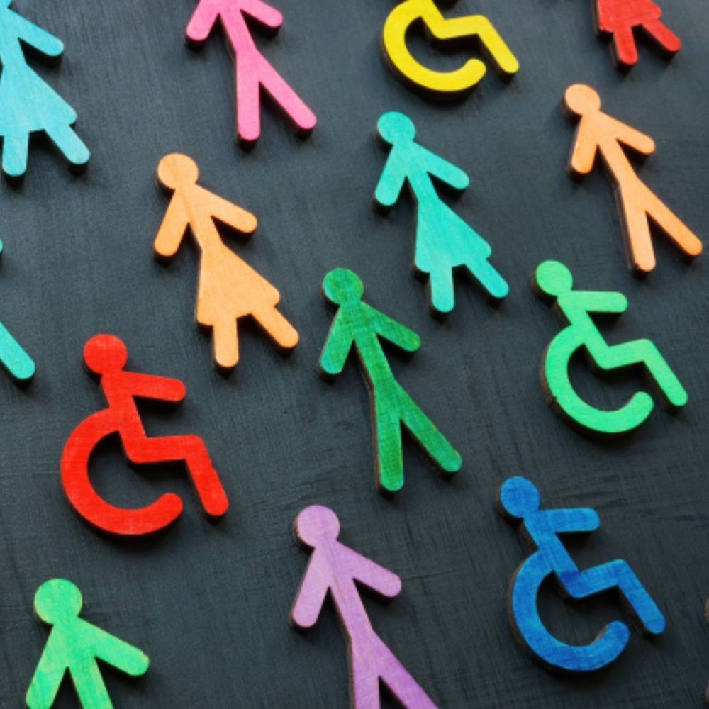 Photograph of wooden figures painted in different colours lying against dark background. Some of the figures are wheelchair users.