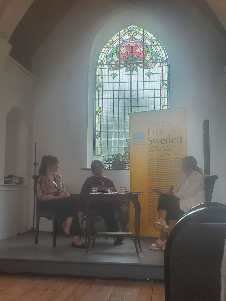 Balsam Karam speaks to an audience in Marino Church from a seat behind a table. Saskia Vogel is to her right
