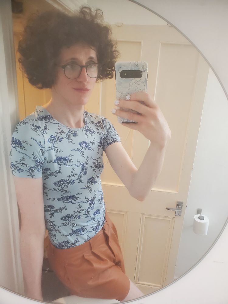 Bathroom mirror selfie of me in a blue T-shirt with a floral design and orange fake-leather shorts