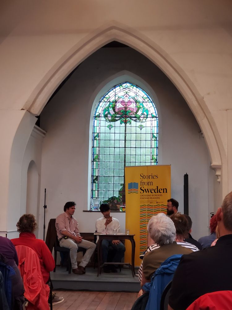 Quynh Tran speaks into a microphone to an audience at Marino Church. Seán Farrell is to his right.