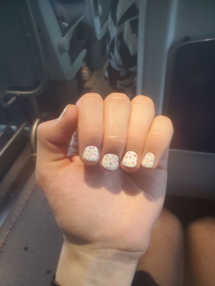 My nails with nail art: a white base with pastel red, blue, and green polka dots.