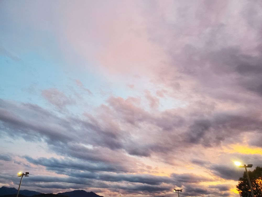 Photo d'un ciel nuageux 
Avec du orange en bas à droite (soleil qui se couche) et des nuages allant du rose pastel au gris, avec des bouts de ciel bleu 
