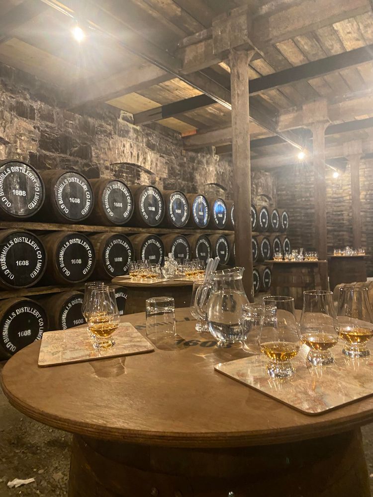 Tables in an old wood ceiling room, set up with whiskey for tasting with barrels in the background.