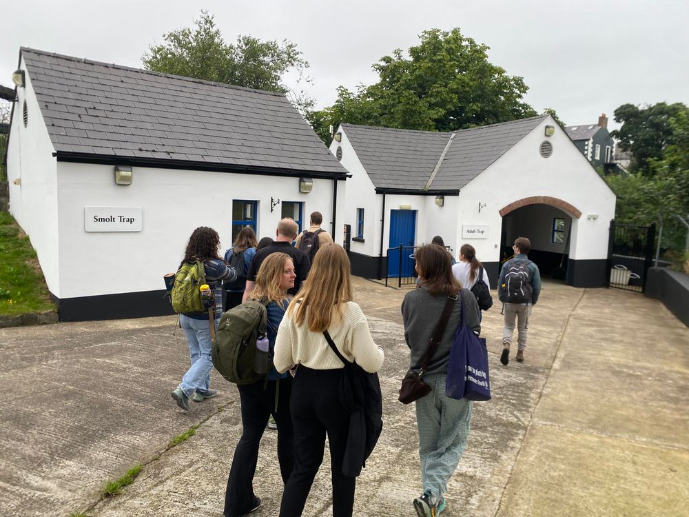 A group of people walk towards two white buildings, one labelled Smolt Trap and one labelled Adult Trap.