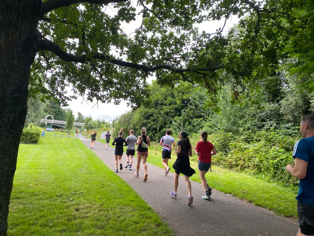 Runners heading away from the camera along a path through a lawned gardens with a bridge in the background