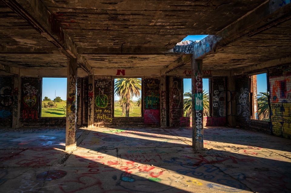 Image of the inside of an abandoned building with graffiti and an open windows exposing a palm tree