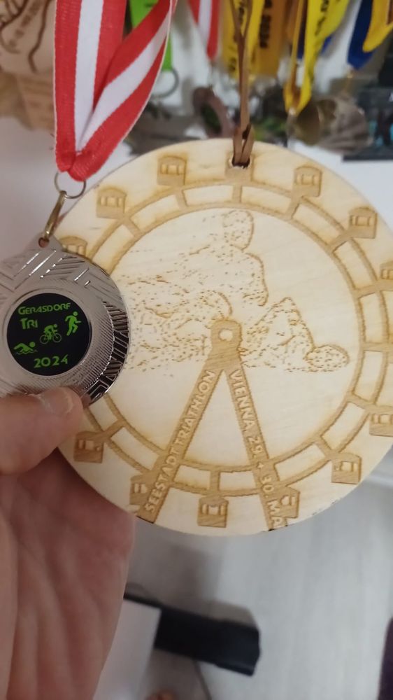 Medaille Gerasdorf-Triathlon. Silber, klein, schwarzer Kern mit grüner Schrift und grünem Schwimmer, Radler, Läufer.

Medaille Seestadt-Triathlon. Holz, sehr groß, mit Riesenrad und stilisierten Schwimmer, Radler, Läufer.