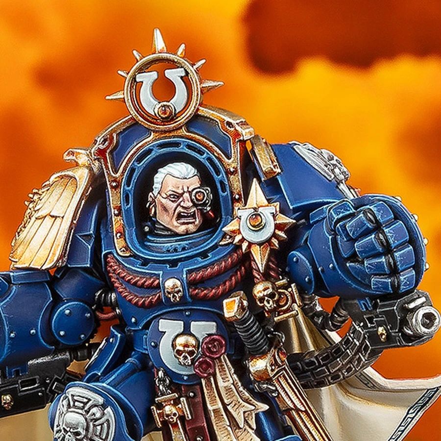 A detailed miniature of Marneus Calgar, a prominent character from the Warhammer 40,000 universe, is depicted in a striking pose. He wears ornate blue power armor adorned with gold embellishments, featuring a prominent Ultramarines symbol on his chest and a skull motif. The background is a dramatic orange, suggesting a fiery battlefield, enhancing the intensity of the scene.