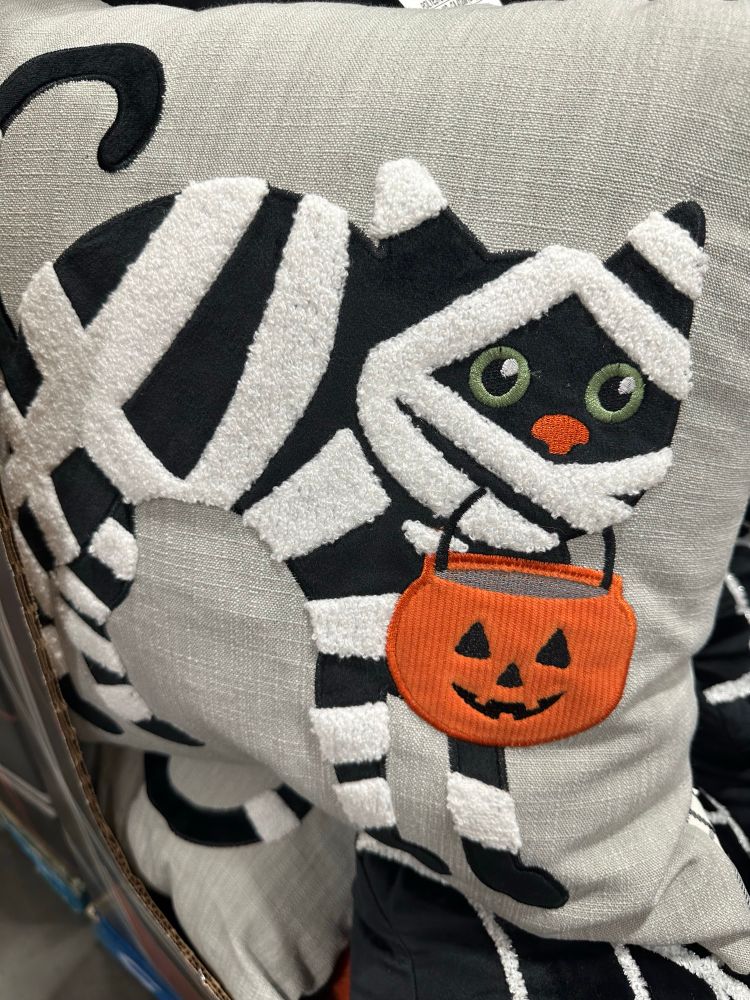 A cute pillow with a mummy cat holding a Halloween bucket in its mouth. 