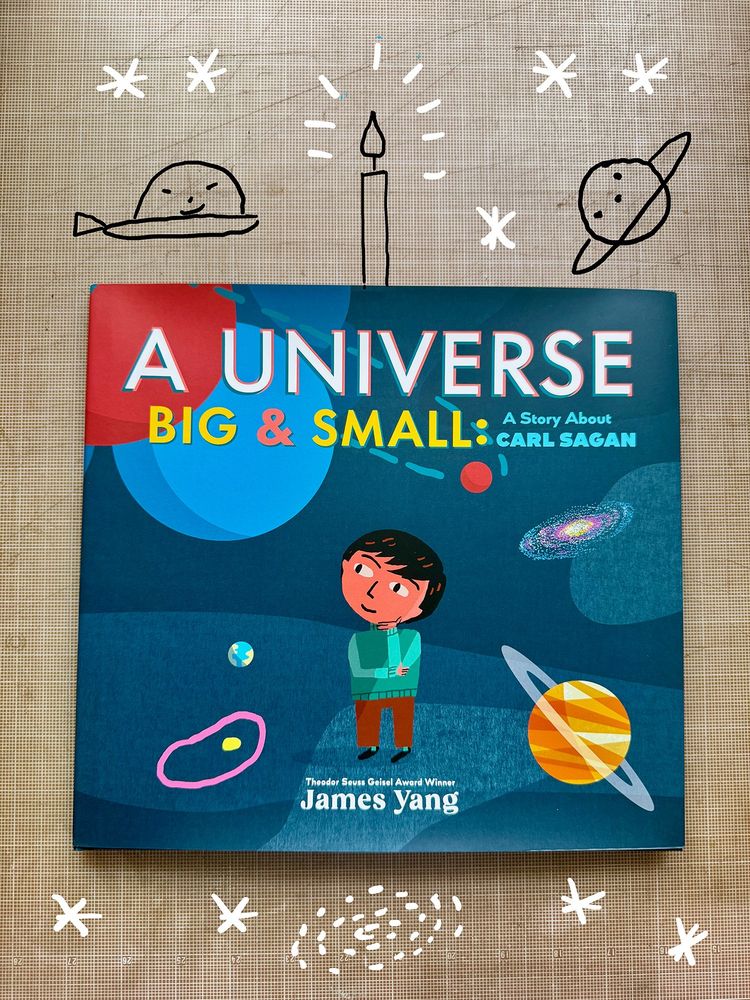 Cover of A Universe Big & Small with a young Carl Sagan surrounded by atoms, cells, and planets with a birthday candle surrounded by stars, a ship, and a planet