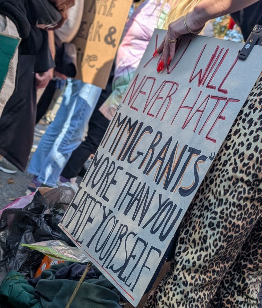 Handwritten cardboard sign "you will never hate immigrants more than you hate yourself".
