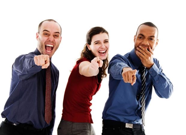 A stock photo of three people in officewear, pointing and laughing with derision and mockery at the camera.