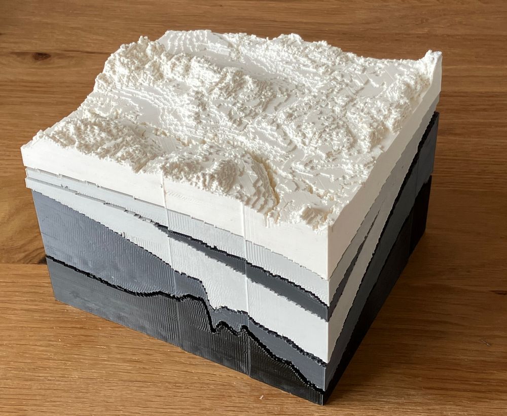 A photograph showing the 3D print of the Minecraft model of Peace River - a cross section of the geological formation of this site in different shades of grey and white to show the layers beneath the surface of the earth.