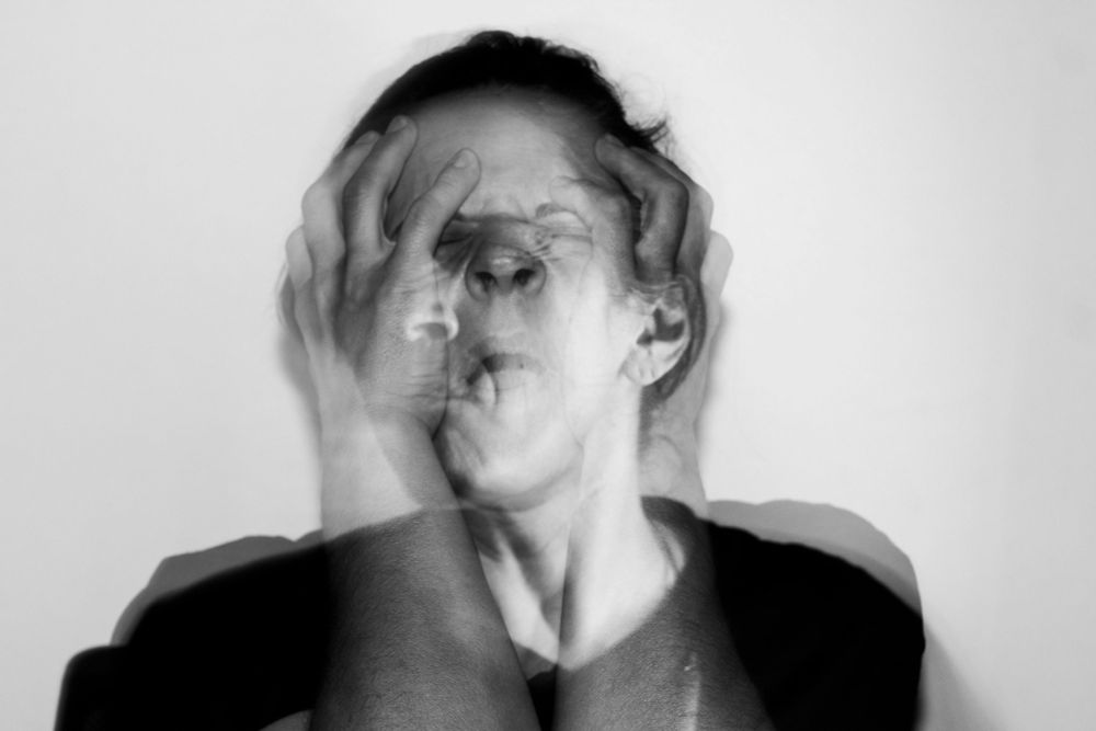 Black and white photo by Adriana Oliveira Correia, of a woman grabbing her head and face with her hands, looking in despair.  Image is purposefully distorted.