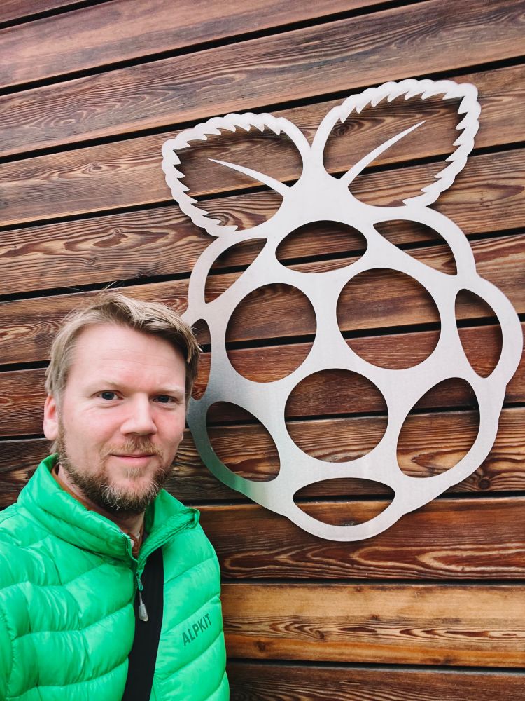 A photo of me standing beside the Raspberry Pi Foundations logo, on the outside of their office building.